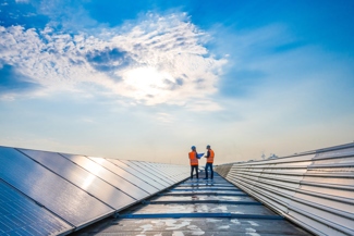 Two men on roof with solar panels, both wearing PPE