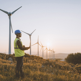 Man stood near windmills, on a hilltop wearing PPE and holding a clipboard